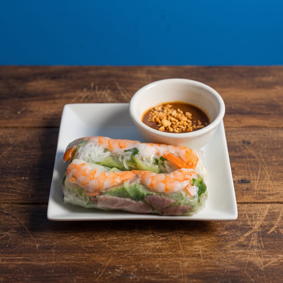 Two fresh spring rolls with shrimp, pork, and vegetables, served with peanut sauce on a white plate.